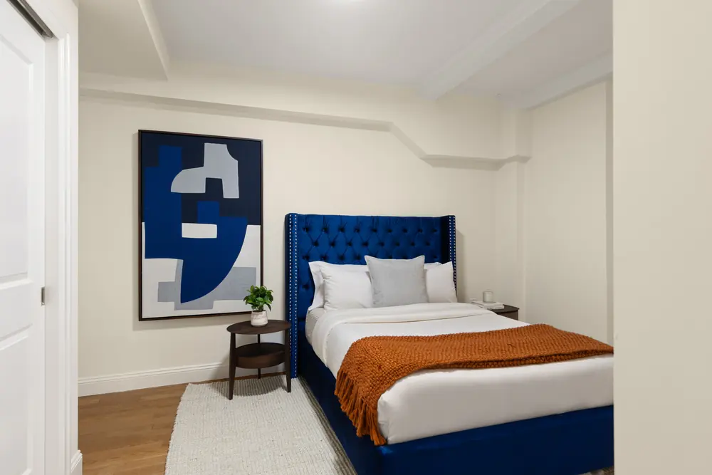 425 Central Park West, Residence 1D: a bedroom with a navy upholstered bed and a graphic blue canvas