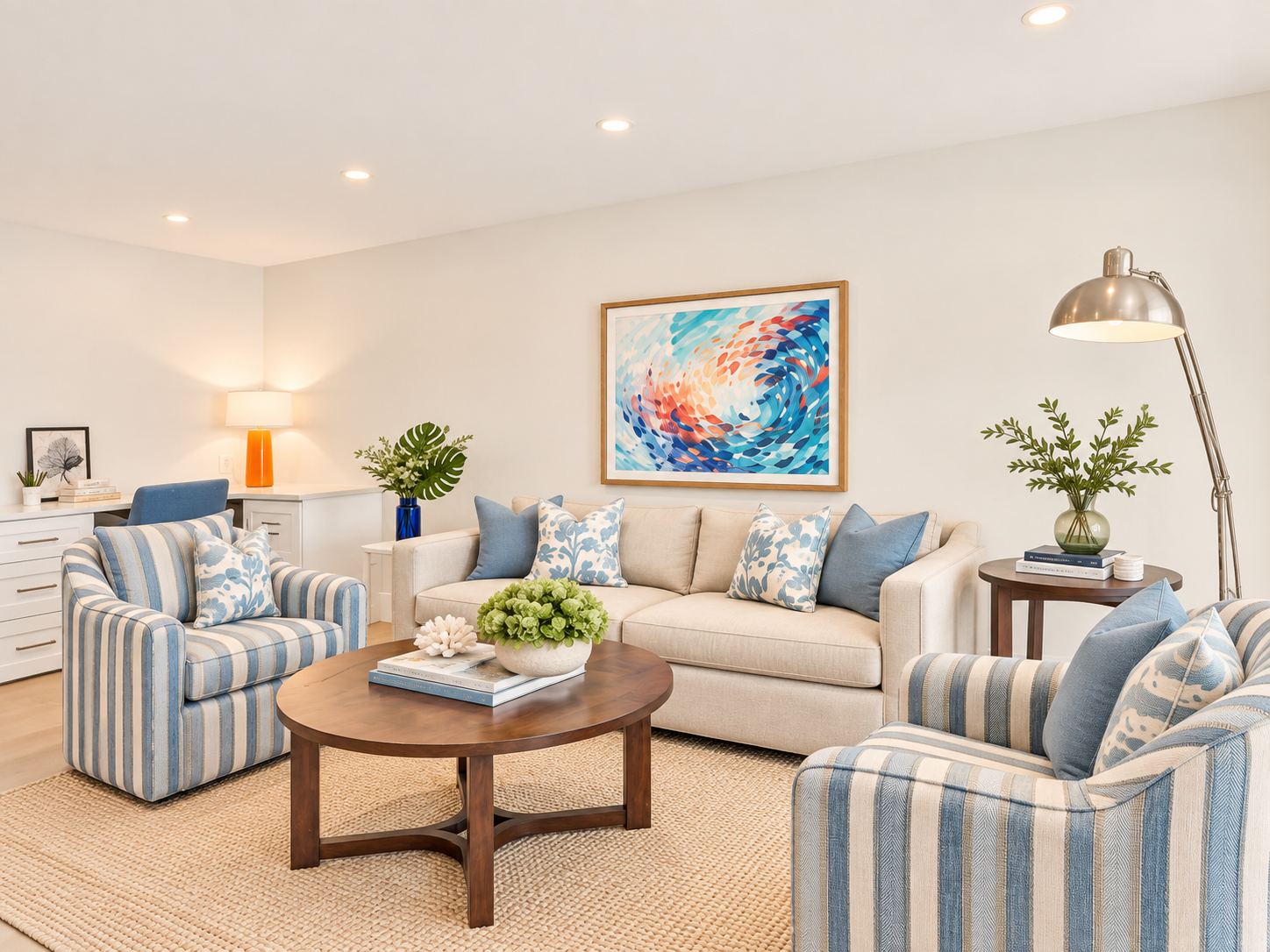 A living room with a cream sofa, blue and white pillows, a round wood coffee table and a colorful wave painting.