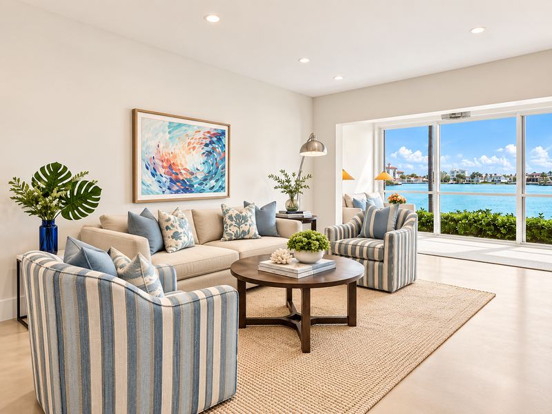 A bright living room with striped armchairs and a round coffee table, sliding glass doors open to the bay.